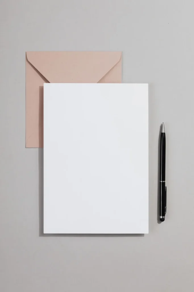 Paper sheet and envelope arranged with a pen on a light surface