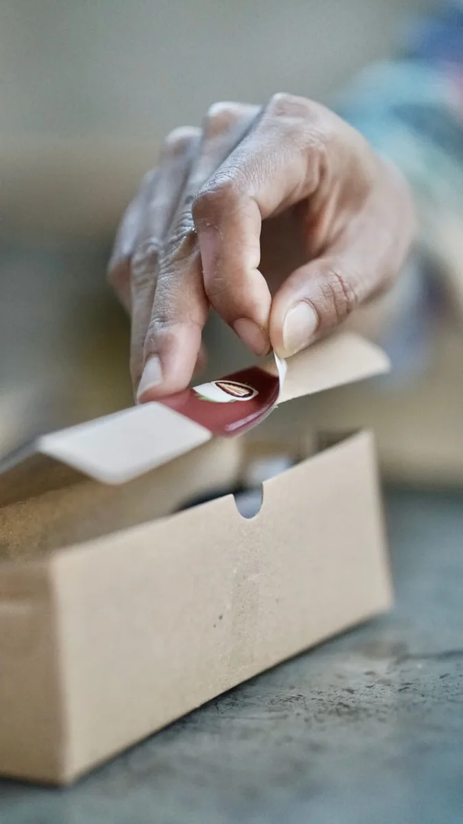 A hand applying a round label to a cardboard package