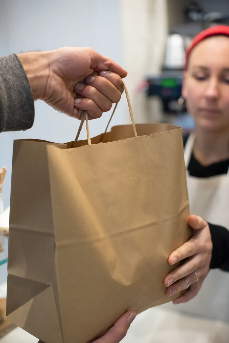 Restaurant worker handing a paper takeaway bag to a customer